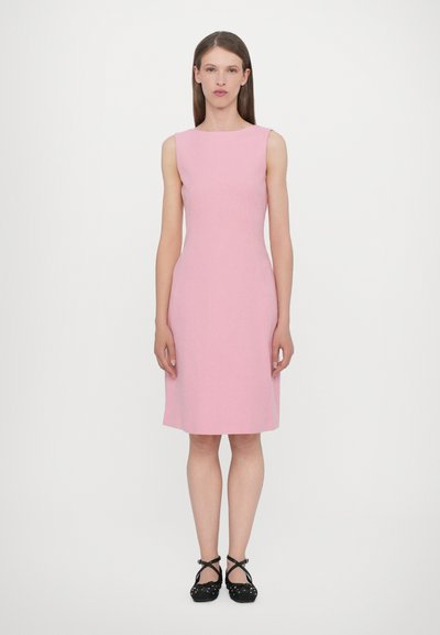 Robe sans manches rose avec un corsage ajusté et une jupe évasée, fabriquée dans un tissu texturé ; associée à des chaussures noires à pois.