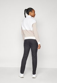 Πουλόβερ σε λευκό, μπεζ και γκρι ύφασμα με ψηλό γιακά· συνδυάζεται με μαύρο παντελόνι. Λεία υφή, αθλητικός σχεδιασμός και εφαρμοστή σιλουέτα.