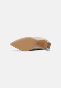 Scarpa con tacco alta beige, con punta affusolata e parte superiore testurizzata. La suola liscia è color cuoio, con una sezione antiscivolo sul tallone.