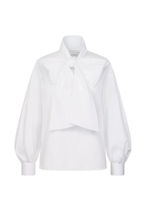 Blouse blanche à manches longues avec larges poignets et un grand nœud noué au niveau du cou, présentée sur un fond uni.