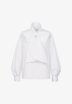 Hvid bluse med lange ærmer, brede manchetter og en stor sløjfe bundet ved halsen, vist på en ensfarvet baggrund.