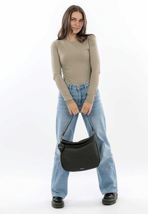 Black leather shoulder bag with a curved shape, top handle, and a heart-shaped tag. Model wears a beige long-sleeve top and light blue jeans.