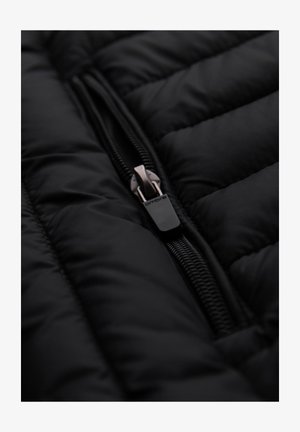 Schwarze Daunenjacke mit einem auffälligen Reißverschluss und metallic-farbenem Ziehgriff sowie strukturiertem, gesteppte Stoff. Glatte Oberfläche, minimalistisches Design.