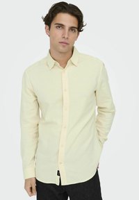 Lichtgele longsleeve shirt met knoopsluiting aan de voorkant, kraag en afgeronde zoom. Gemaakt van een zacht materiaal met een subtiele textuur. Zwarte label aan de zoom.