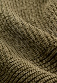 Olivovo zelený pletený textil so štruktúrovaným rebrovaným vzorom a viditeľnými stehmi, ktorý vytvára hĺbku a jemnosť.