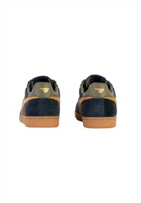 Baskets en daim bleu avec des accents beige, design minimaliste, semelle en caoutchouc et un petit logo doré près du talon. Vue arrière affichée.