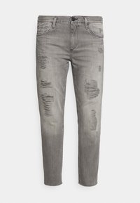 Jeans de mezclilla gris con corte ajustado, que presentan múltiples parches desgastados y decoloración. Diseño estándar de cinco bolsillos con cremallera y cierre de botón.