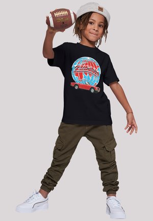 Black t-shirt features graphic of a red car and globe in blue and red, paired with olive green cargo pants and white sneakers.