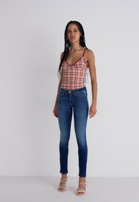 Top corto de cuadros rojos y blancos con tirantes finos y detalle de botones, combinado con jeans ajustados azules y sandalias blancas con tiras.