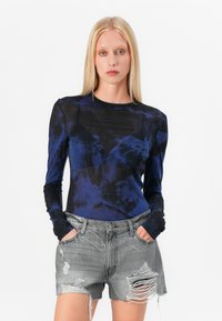 Chemise à manches longues en tie-dye bleu foncé avec un col rond, accompagnée d'un short en denim gris déchiré avec des bords effilochés et des poches.