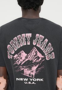 Sort bomulds T-shirt med et stort pink grafik af bjerge og en vogn samt teksten "TOMMY JEANS NEW YORK U.S.A." på ryggen.