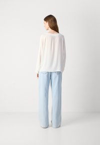 Witte blouse met lange mouwen, een losse pasvorm en een geplooid achterdetail, gecombineerd met lichtblauwe, wijde denim jeans. Glad stoftextuur.