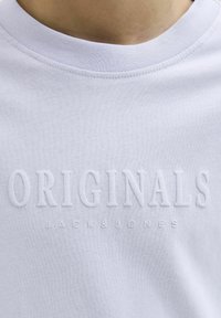 Balta medvilninė marškinė su apvalia iškirpte, su iškilmingai užrašu "ORIGINALS JACK & JONES" šiek tiek pakeltu, toniniu dizainu.