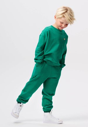 Sweatshirt en coton vert et joggers assortis, avec une coupe décontractée, des poignets côtelés et des poches latérales. Assortis avec des baskets montantes blanches.