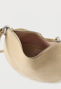 Beige suède handtas met een gebogen vorm, zilveren rits en leren binnenkant. Voorzien van een schouderriem voor gemakkelijk dragen. Eenvoudig en modern design.