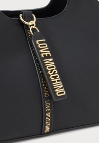 Zwarte leren tas met een gouden rits en een gegraveerd label met de tekst "LOVE MOSCHINO" in reliëfletters.