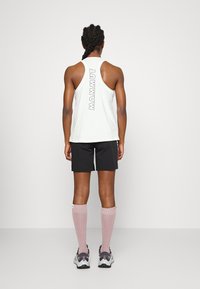 White tank top with "MAMMUT" graphic at the back, paired with black shorts and pink knee-high socks. Sneakers have gray and white accents.