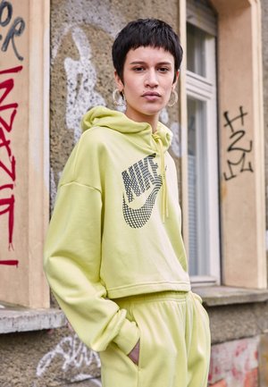 Limegrön croppad huvtröja med svart Nike-logga, kombinerad med matchande sweatpants. Har en dragsko i huven och lös passform.