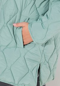 Ljusgrön vadderad jacka med diamantmönster, sidoficka och avslappnad passform med ett strukturerat, vattenavvisande yttertyg.