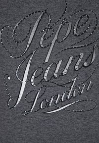 Šedé tričko s dekorativním textovým designem v lesklé stříbrné barvě a akcenty z kamínků, na kterém je nápis "Pepe Jeans London." Hladká textura.