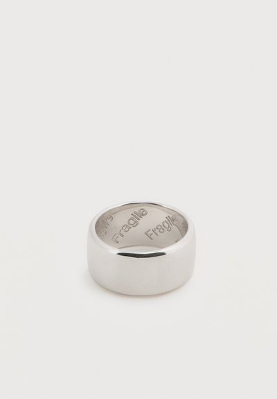 Ευρύ ασημένιο δαχτυλίδι με λεία επιφάνεια, χαραγμένο στο εσωτερικό με τη λέξη «Εύθραυστο» επαναλαμβανόμενη πολλές φορές.