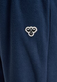 Marinblå fleecebyxor med en texturerad yta, med en dekorativ broderad design av en vit och svart bi på vänster sida.