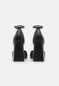 Chaussures à talons hauts en cuir noir avec un talon carré, une sangle à la cheville, un dos fermé et un design à bout ouvert. Texture lisse, style minimaliste.