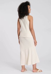 Crème-kleurige mouwloze top en lange aansluitende rok van gestructureerde stof, met een uitlopende zoom en minimale naaddetails. Sandalen complementeren de outfit.