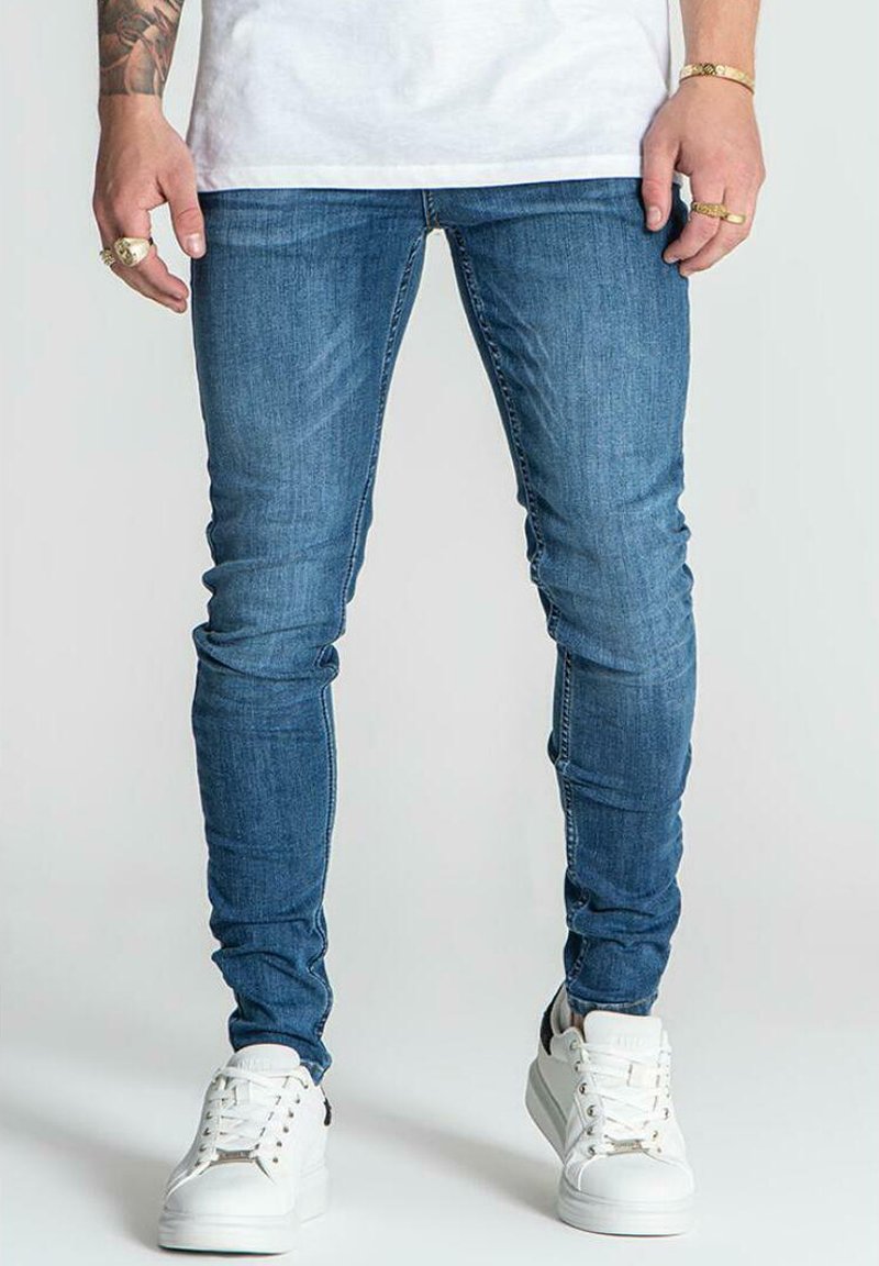 Jeans in denim blu a vestibilità slim con una superficie liscia, caratterizzati da un classico design a cinque tasche e dettagli vissuti. Abbinati a sneaker bianche.
