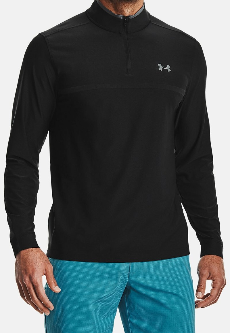 Pullover noir à manches longues avec un col zippé quart, présentant une texture lisse et des détails subtils sous les bras, associé à un short bleu texturé.