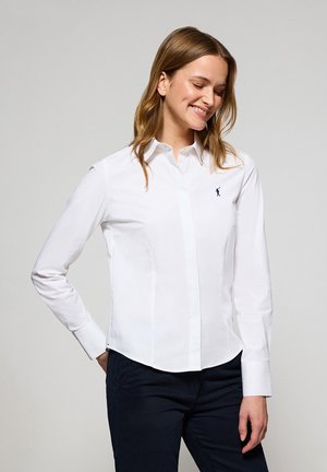 Camicia bianca a maniche lunghe, design fitted e un piccolo logo blu sul petto. Tessuto di cotone liscio, colletto classico.