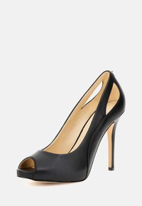 Svart läder högklackade peep-toe pumps med utskurna sidor och beige inredning, visade mot en vit bakgrund.