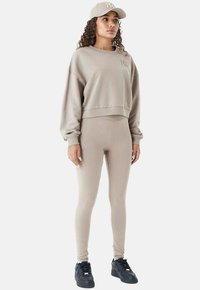 Sweatshirt beige à manches courtes avec des leggings assortis, le tout fabriqué en matériau doux. Comprend une casquette, portée avec des baskets noires. Détails brodés subtils sur le haut.