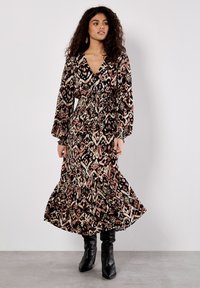 Maxikleid mit einem abstrakten Muster in Schwarz, Pink und Creme, langen Puffärmeln, tailliertem Bund und einem volantrimierten Saum. Kombiniert mit schwarzen Stiefeln.