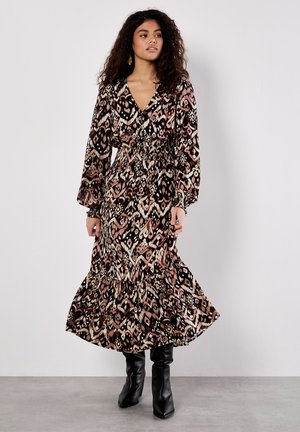 Maxikleid mit einem abstrakten Muster in Schwarz, Pink und Creme, langen Puffärmeln, tailliertem Bund und einem volantrimierten Saum. Kombiniert mit schwarzen Stiefeln.