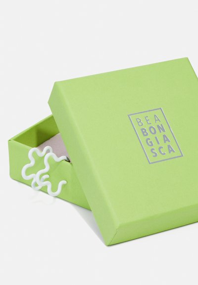 Zeleni papirnati okvir sa srebrnim logotipom na vrhu, blago otvoren kako bi otkrio bijeli, skulpturalni akcent unutra.