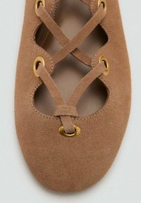 Balerini din suede maron cu un design în cruce, ochiuri aurii și un interior neted. Vârf rotund și formă minimalistă.