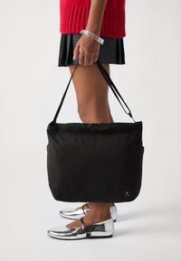 Svart tote bag med en glatt, matt finish og justerbare skulderstropper. Har en sidelomme og en glidelås på toppen.