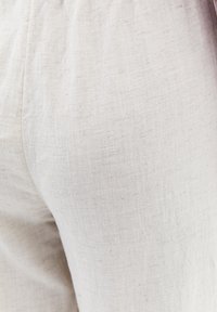 Pantalons en lin beige clair avec une surface texturée et une taille élastique, affichant de subtiles variations de tissu. Pas de motifs ou d'accents visibles.