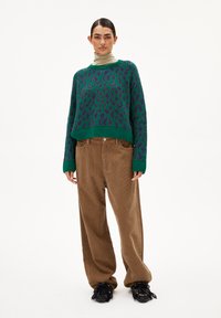 Grüner und lila Leopardenmuster-Pullover mit einem cropped Design, kombiniert mit braunen Corduroy-Hosen mit weitem Bein und schwarzen Schuhen mit Franzen.