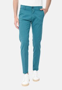 Chino turchesi con vestibilità slim, realizzati in cotone, con chiusura a bottone e tasche laterali, abbinati a sneakers bianche.