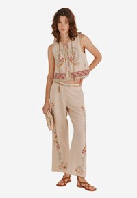 Un ensemble en lin beige composé d'un haut brodé court et d'un pantalon brodé ample. Mettant en valeur des motifs floraux colorés.
