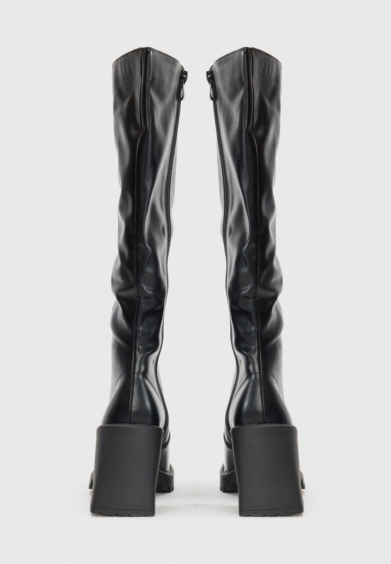 Bottes en cuir noir jusqu'au genou avec une texture lisse, dotées d'un morceau de talon carré et d'une fermeture éclair sur toute la longueur à l'arrière.
