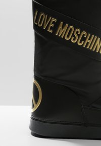 Schwarzer High-Top-Sneaker mit glänzender Oberfläche, ausgestattet mit einem breiten schwarzen Riemen, auf dem "LOVE MOSCHINO" in goldener Schrift steht, sowie einem goldfarbenen Akzent-Logo.