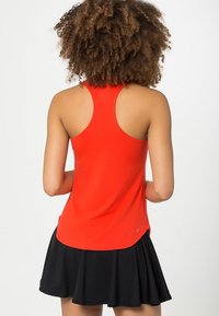 Rode sportieve tanktop met een racerback ontwerp, gecombineerd met een zwarte uitlopende rok. Gladde textuur; logo detail op de zoom van de tanktop.