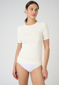 Short-sleeve cream top with a round neckline, soft texture, fitted design, and subtle seams. Worn with white bikini bottoms.