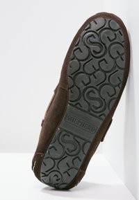 Pantofole in suede marrone con suola in gomma texturizzata caratterizzata da un motivo circolare e logo impresso. Design a profilo basso, con apertura sul retro per una vestibilità facile.