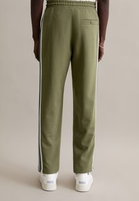 Olijfgroene joggingbroek met elastische tailleband, zijstrepen en een achterzak met knoop. Gecombineerd met witte sneakers.