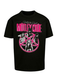 Černé bavlněné tričko s růžovou a bílou grafikou členů kapely uvnitř pentagramu a textem, který říká „Shout at the Devil“ a „MÖTLEY CRÜE.“