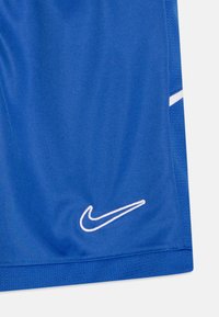 Siniset urheilushortsit, joissa on valkoinen Nike-swoosh-logo brodeerattuna lähelle helmaa ja valkoinen raita sivusaumassa.